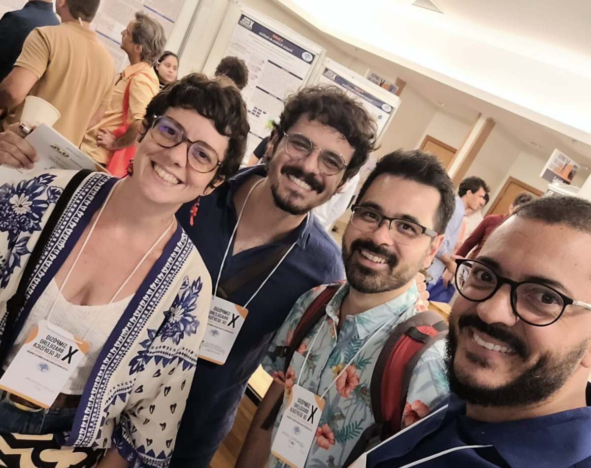 A woman and three men smiling with people at a poster session in the background